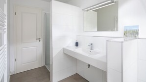 Un baño con puerta blanca, ducha, lavamanos y espejo.