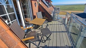 Varanda com mesa, cadeiras, porta de vidro e vista para o mar.