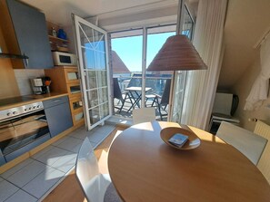 Eine moderne Küche mit Essbereich, großen Schiebeglasfenstern zum Balkon und Blick auf die Nachbarschaft.