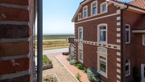 Een gebouw van baksteen met een rode dakbedekking, een geplaveid pad en uitzicht op een vlak landschap.