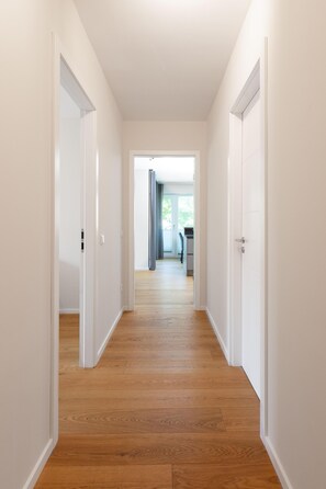 A hallway with wooden flooring, white walls, and doors leading to a room with a window and a desk. - Experience unforgettable moments in the charming Villa Sohn Deck7! (Juist)