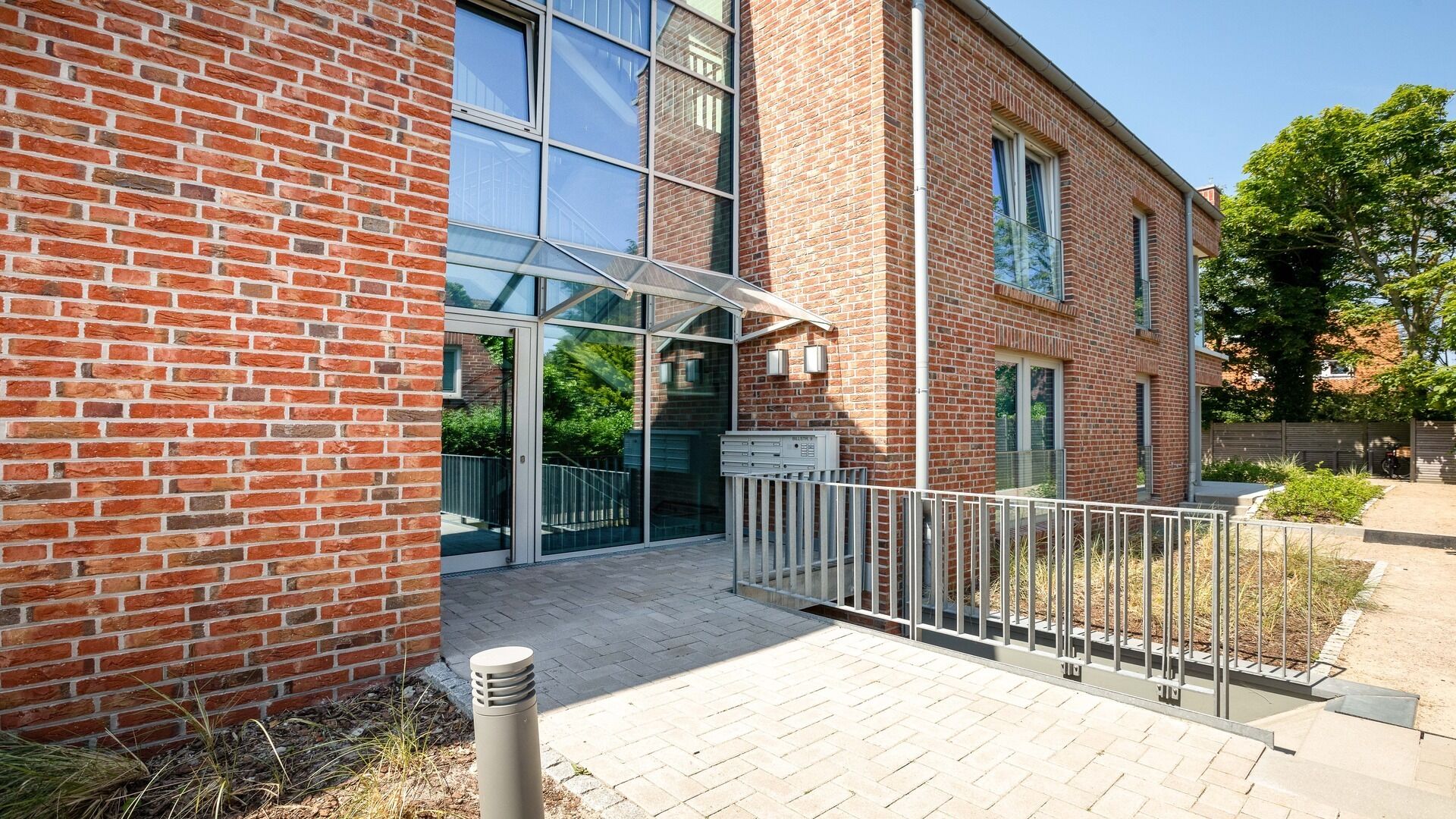 A brick building with a glass entrance, a metal fence, and a paved walkway.
