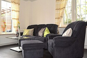 A modern living room with a sectional sofa, a coffee table, and a view of the outdoors through large windows. - Cozy vacation apartment near the center (Juist)