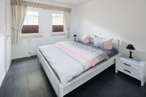 A bedroom with a bed, two bedside tables, a window with curtains, and a radiator. - Cozy vacation apartment near the center (Juist)