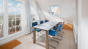 Ein moderner Essbereich mit einem großen Tisch, blauen Stühlen und großen Fenstern mit Vorhängen.
