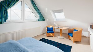 Ein Zimmer mit einem Bett, zwei Korbstühlen, einem kleinen Tisch und einem Fenster mit Vorhängen.
