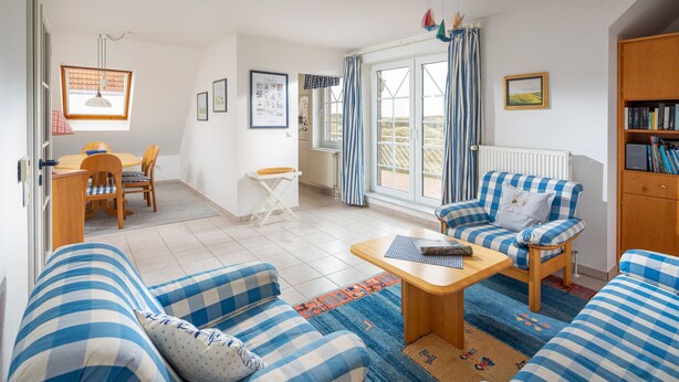 Een woonkamer met geruite banken, een houten salontafel en een eethoek met een tafel en stoelen.