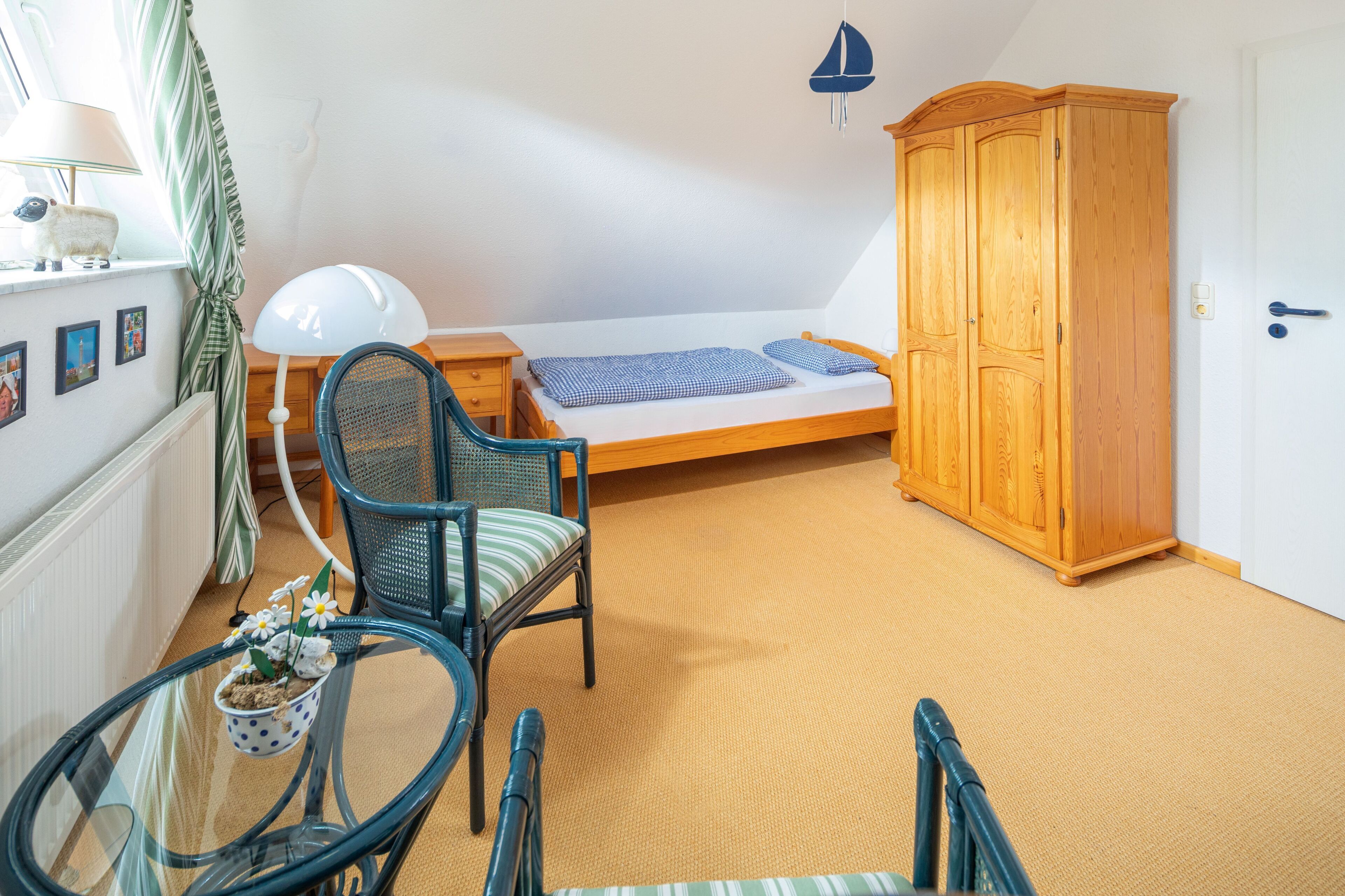 Una habitación pequeña con una cama, un armario de madera, una silla, una mesa con una planta en maceta y una lámpara.