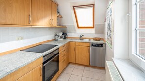 Een keuken met houten kastjes, een inbouwoven, een vaatwasser, een raam en een betegelde spatwand.