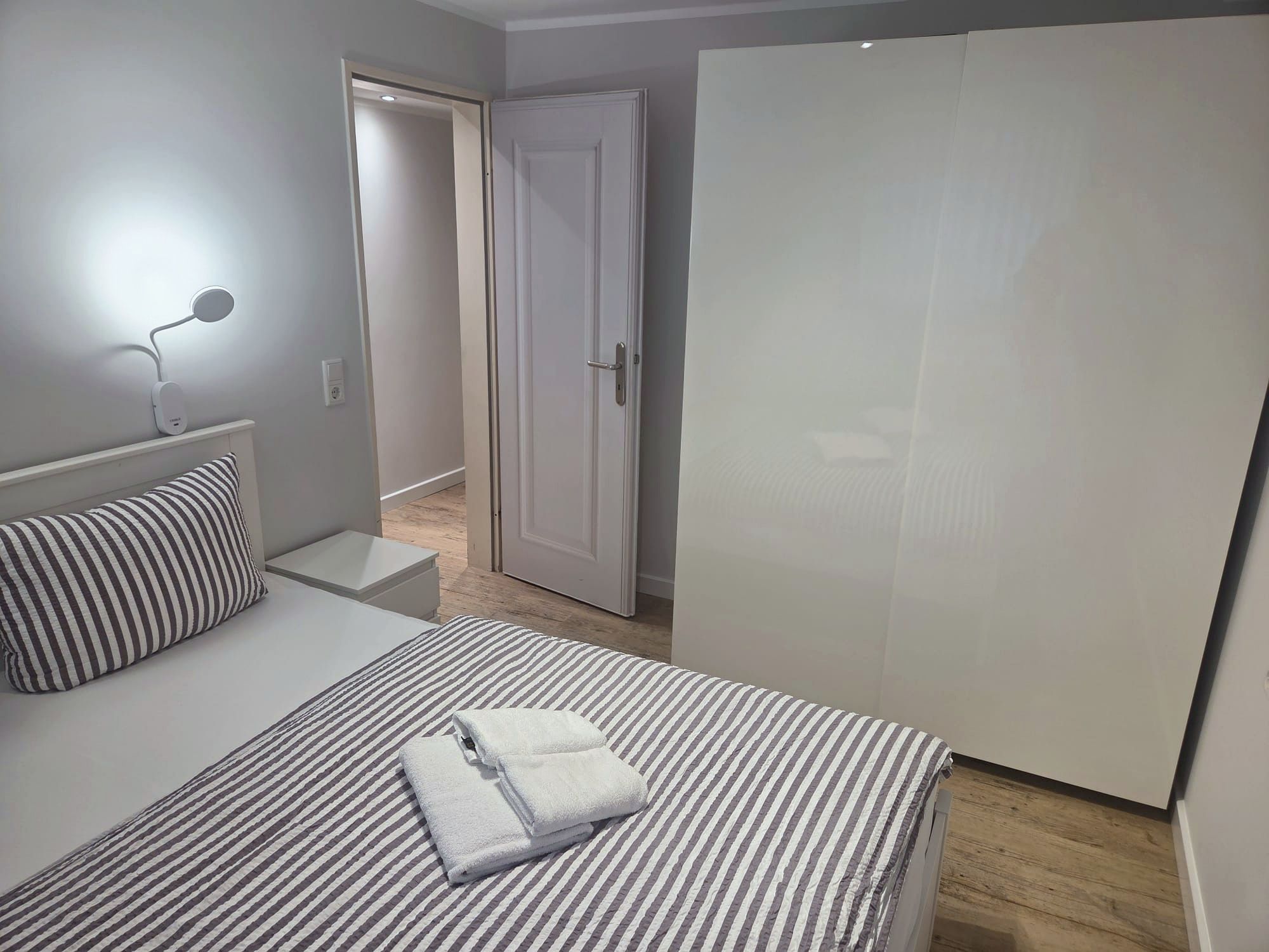A bedroom with a bed, a bedside table, a lamp, a striped pillow, and a wardrobe.