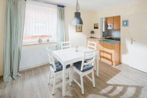 A dining area with a white table and chairs, a kitchen with wooden cabinets, and a window with curtains. - "Idyllic vacation apartment Seute Deern Kajüte - your perfect retreat on the (Juist)