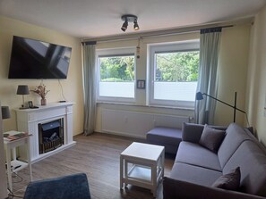 A living room with a flat-screen TV, fireplace, sofa, and a small table. - "Idyllic vacation apartment Seute Deern Kajüte - your perfect retreat on the (Juist)