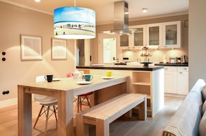 Cocina moderna con una mesa de madera, taburetes de bar, un banco y una lámpara colgante con una escena de playa.