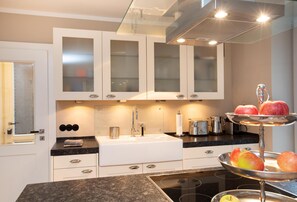 Una cocina moderna con gabinetes blancos, encimera de granito, pileta de acero inoxidable y un frutero de tres niveles.