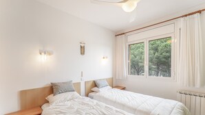 A bedroom with two beds, a nightstand, a wall-mounted light, a window with curtains, and a radiator. - Holiday Home 'Pineda 12' with Mountain View, Private Pool and Wi-Fi (Pals)