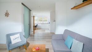 Ein modernes Wohnzimmer mit grauem Sofa, blauem Sessel und Couchtisch aus Holz.