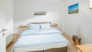 Ein Schlafzimmer mit einem Bett, Nachttischen, einem hölzernen Hocker und zwei Wandbildern.