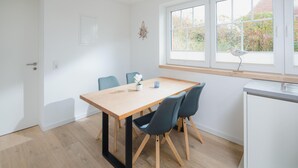 Eine moderne Küche mit Holztisch und -stühlen, einem weißen Kühlschrank und einem Fenster mit Blick ins Grüne.