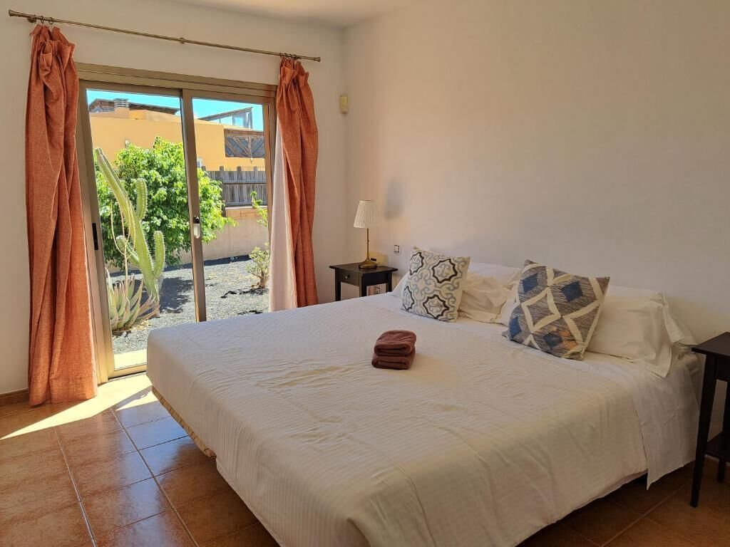 Une chambre à coucher avec un lit, des rideaux, une table de chevet et une vue sur l’extérieur, accessible par une porte coulissante.