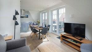 A modern living room with a TV, sofa, and dining area with chairs and a table. - Modern vacation apartment for 4 people, new building near the beach (Juist)