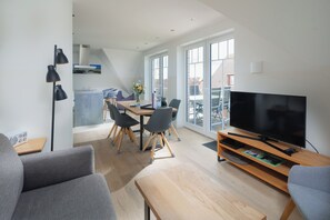 A modern living room with a TV, sofa, and dining area with chairs and a table. - Modern vacation apartment for 4 people, new building near the beach (Juist)