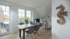 A modern dining area with a wooden table, chairs, and a large window. - Modern vacation apartment for 4 people, new building near the beach (Juist)