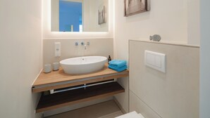 A modern bathroom with a large oval sink, a mirror, and a wooden vanity. - Modern vacation apartment for 4 people, new building near the beach (Juist)