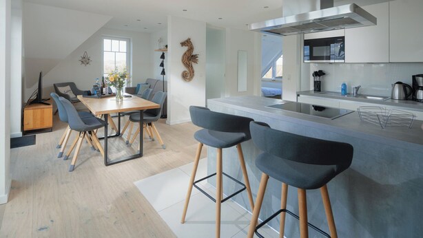 A modern kitchen with a central island, bar stools, and a dining area with a table and chairs. - Modern vacation apartment for 4 people, new building near the beach (Juist)