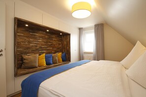 A bedroom with a large bed, a wooden accent wall, a window with curtains, and a ceiling light. - Centrally located apartment for 4 people with sea view (Juist)