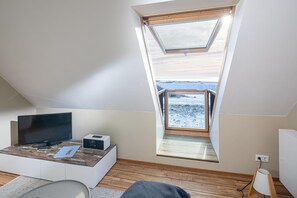 A room with a sloped ceiling, a television on a wooden table, a small white cabinet, a lamp, and a view of a snowy landscape through a skylight. - Centrally located apartment for 4 people with sea view (Juist)