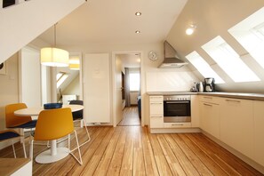 A modern kitchen with wooden flooring, a dining area with orange chairs, and skylights. - Centrally located apartment for 4 people with sea view (Juist)