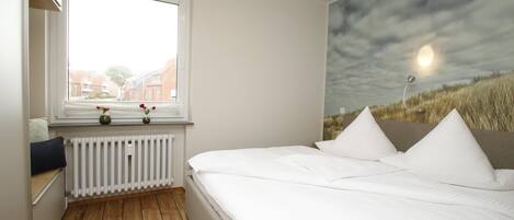 Een slaapkamer met een bed, een raam, een radiator en een muurschildering.