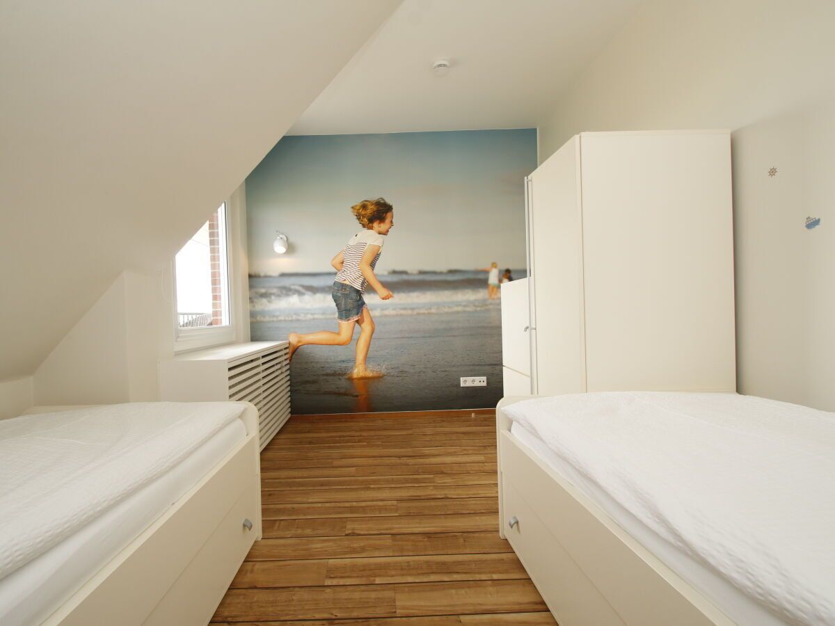 A room with two beds, a wooden floor, a wall mural of a beach, and a window.