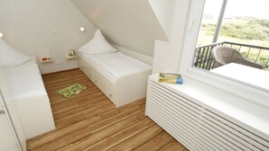 Ett litet, kompakt rum med ett sluttande tak, en säng, ett litet bord och ett fönster med utsikt över grönområden.