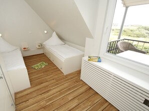 A small, compact room with a sloped ceiling, a bed, a small table, and a window with a view of greenery. - "Relaxation and sea views: Your perfect vacation in Juist awaits you!" (Juist)