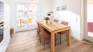 Een eetruimte met een houten tafel, stoelen, een vaas met bloemen en uitzicht door een glazen deur op een terras.
