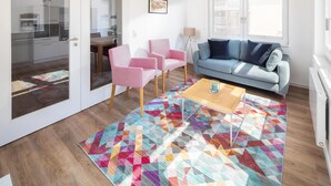 Een woonkamer met een bank, stoelen, een salontafel en een kleurrijk vloerkleed.