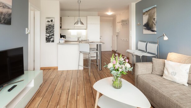 A modern living room with a flat-screen TV, a white coffee table, a beige sofa, and a vase with flowers. - Centrally located vacation apartment for 3 people (Juist)