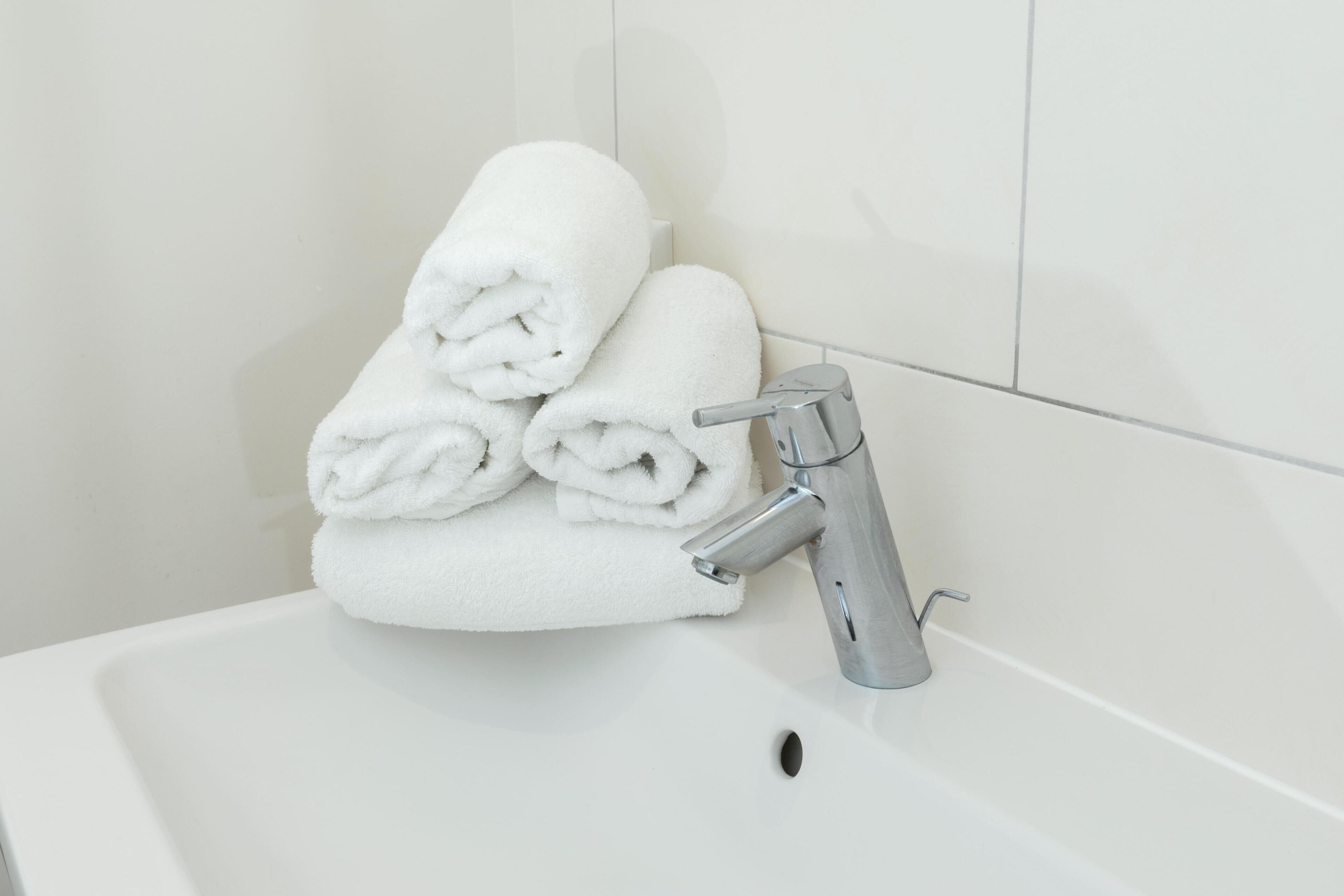 A white bathroom sink with a silver faucet and a stack of white towels.