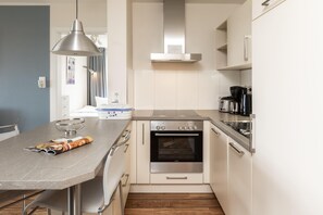 A compact kitchen with a built-in oven, a coffee maker, and a dining area with a bowl and magazine. - Centrally located vacation apartment for 3 people (Juist)