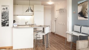 A modern kitchen with white cabinets, a central island, bar stools, a hanging light fixture, and a painting on the wall. - Centrally located vacation apartment for 3 people (Juist)