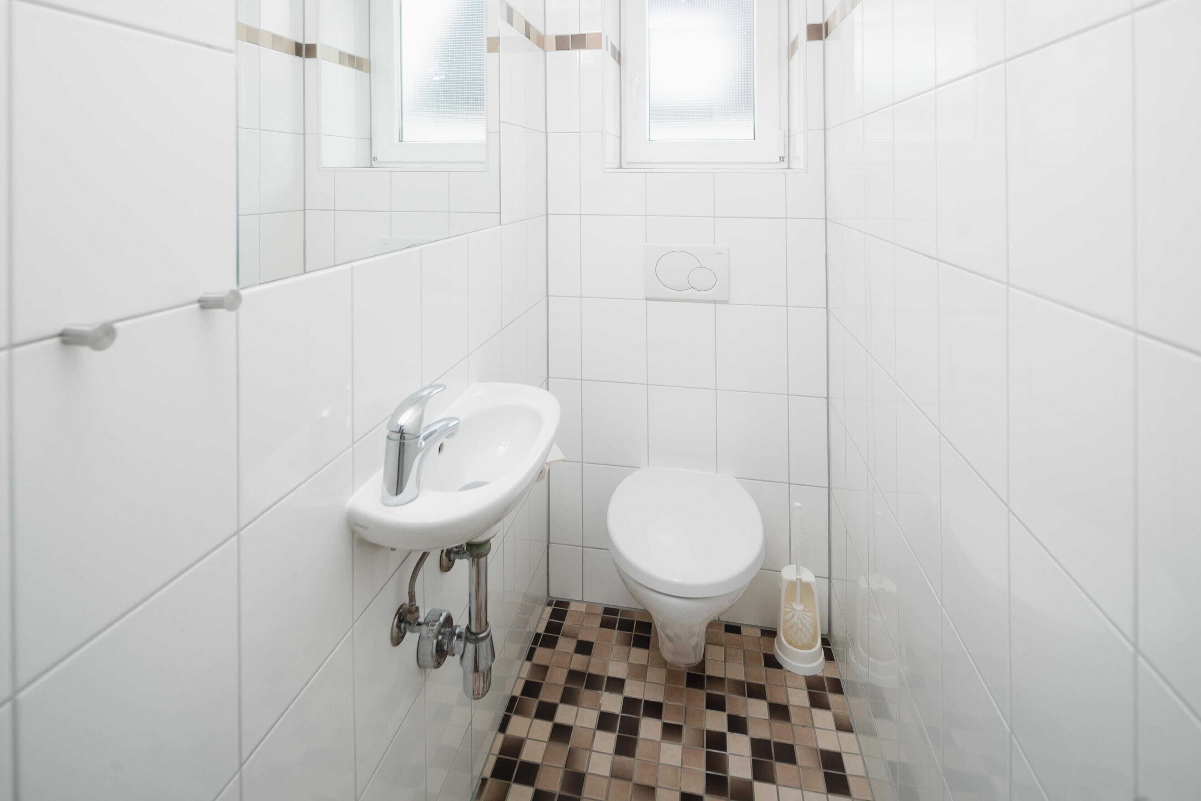 Ein Badezimmer mit weißen Fliesenwänden, einem weißen Waschbecken, einer weißen Toilette und einem Schachbrettfußboden.