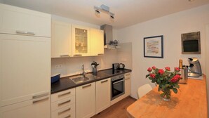 A modern kitchen with white cabinets, a black countertop, a built-in oven, and a coffee machine. - Cozy vacation apartment close to the beach (Juist)