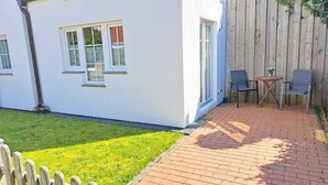A white building with a brick patio, a wooden fence, and two chairs. - Cozy vacation apartment close to the beach (Juist)