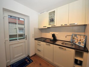 A compact kitchen with white cabinets, a black countertop, a coffee maker, and a decorative tile backsplash. - Cozy vacation apartment close to the beach (Juist)