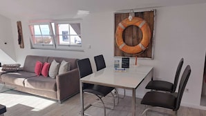 A modern living room with a sofa, chairs, a table, a wooden wall decor, and a window. - Cozy vacation apartment close to the beach (Juist)