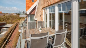 Un balcón con mesa y sillas, que da a un jardín y un edificio de ladrillo.