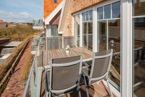 A balcony with a table and chairs, overlooking a garden and a brick building. - Modern vacation apartment for 4 people, new building near the beach (Juist)