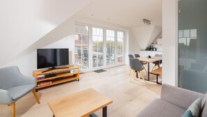 Una sala de estar moderna con una televisión de pantalla plana, un sofá, una mesa de centro y un comedor con sillas y una mesa.