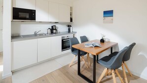 Ett modernt kök med vita skåp, en mikrovågsugn och en kaffebryggare. Där finns ett matbord med stolar och en bok.